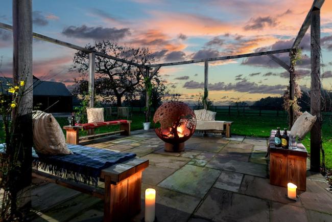 Outdoor seating surrounds a burning firepit at dusk