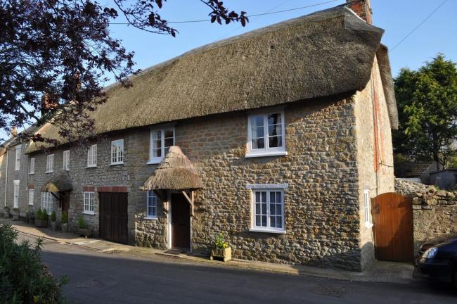 An old stone walled thatched holiday cottage positioned next to a road.
