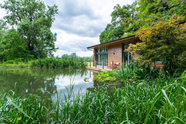 A holiday home sits on the edge of a lake surrounded by trees.