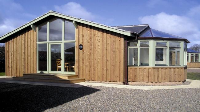 A contemporary wood-clad bungalow with floor-to-ceiling windowsurrounded by a shingled garden.