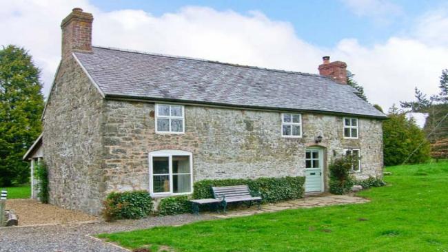 A long, stone-built Shropshire cottage surrounded by a large hedge-lined lawn