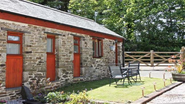 A single storey, stone barn conversion overlooks a lawned garden with outdoor table and chair.