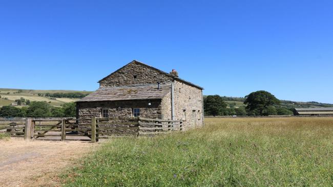A fenced-in stone-built barn conversion is surrounded by open fields
