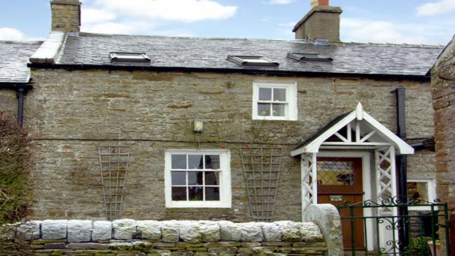 A terraced stone cottage with a low wall around the front garden