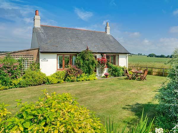 A holiday bungalow with a flowerbeds and a lawn surrounded by open fields.