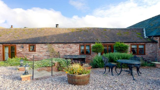 A single-storey barn conversion overlook a shingled courtyard with a shrub-filled flower bed.
