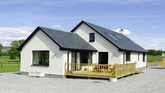 A chalet bungalow with a large fenced-in deck is surrounded by open countryside.