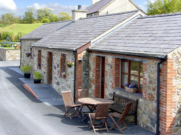 A single storey, Gwynedd barn conversion in a courtyard with outdoor tables and chairs.