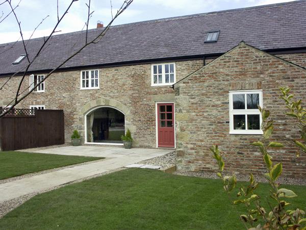 Two-lawns and a path ead to a stone-built terraced cotage with a foor-to-ceiling wide front window.