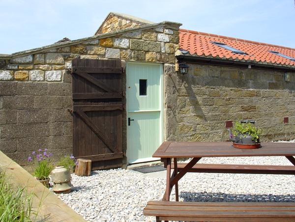 Entrance to a single storey seaside barn conversion in front of which is a wooden picnic table.