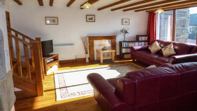 Interior of a spacious pine-floored lounge with pine beams, rugs and large sofas.