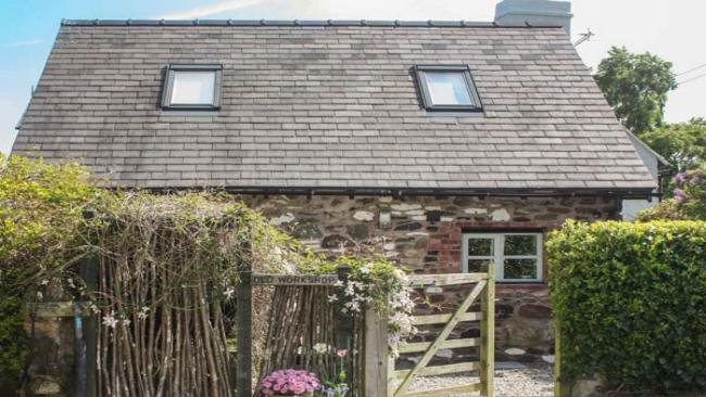 A brick-built barn conversion in Shropshire sits behnd a hedge and a tall, rose covered picket fence