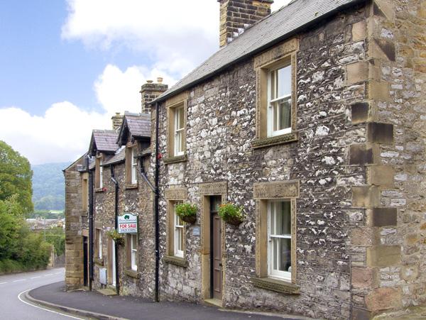 a double-fronted, stone-built terraced cottage on an empty street.