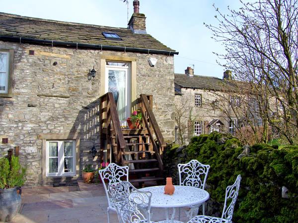 A stone barn conversion with steps to a 1st floor enntrnce from a patio with table and chairs.