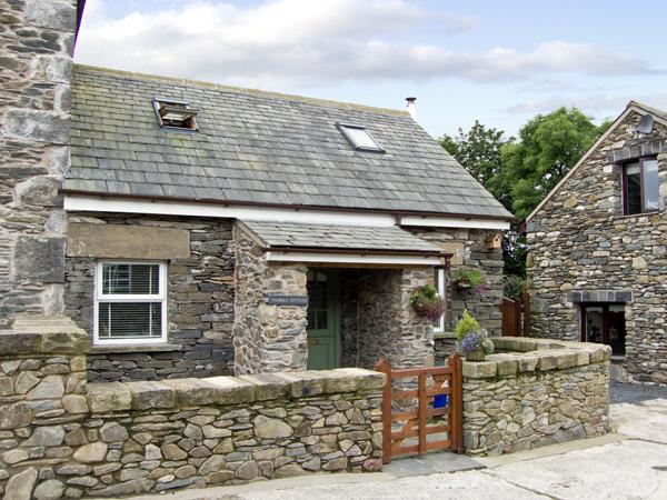 A 2-storey holiday cottage in Ulverston in a converted stone barn surrounded by a low stone wall.