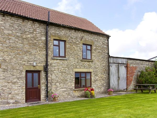 A stone-built, 2-storey holiday cottage in Helmsley overlooking a large lawn.