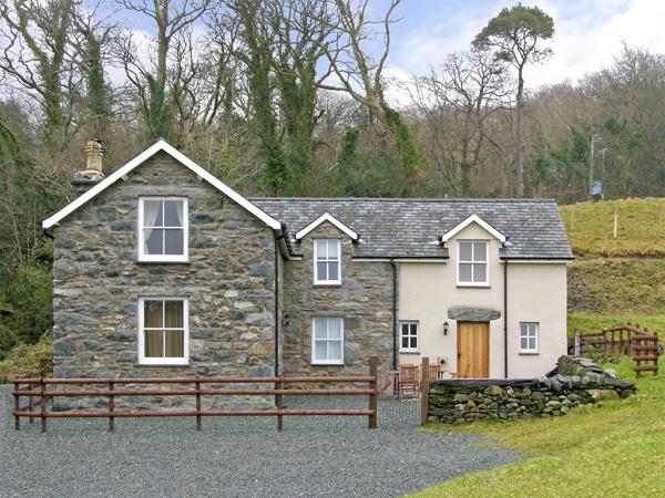 A large slate roofed Lake district holiday cottage its in front of a line of tall tres.