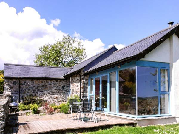 Exterior of a single-storey, stone barn conversion with a contemporary wood and glass extension.