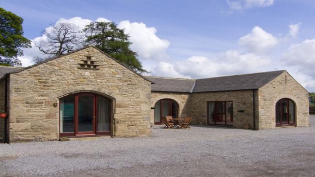 A U-shaped, stone barn conversion with floor-to-ceeiing windows looks out over a large shingled courtyard.