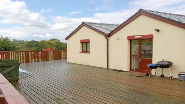 Twin gabled exterior of a bungalow with a feenced-in, large wooden deck for BBQs surrounding it.