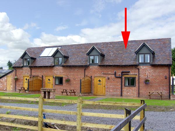 An end-of-terrace, brick holiday cottage in Church-Stretton behind a front lawn.