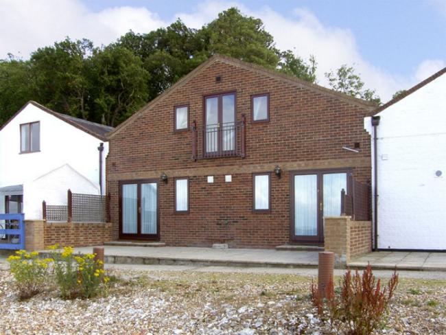 A wide 2-storey gable end of an Isle-of-Wight holiday cottage with floor-to-ceiling windows.