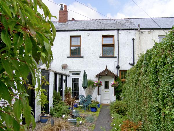 A 2-storey, stone-built gwynedd holiday covvage oveerlooks a garden full of poptted plants and shrubs.