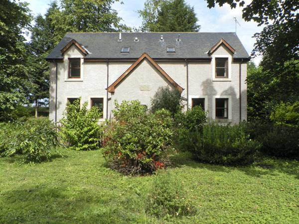 A double-fronted holiday cottage witha covered porch overlooks a mature front garden.