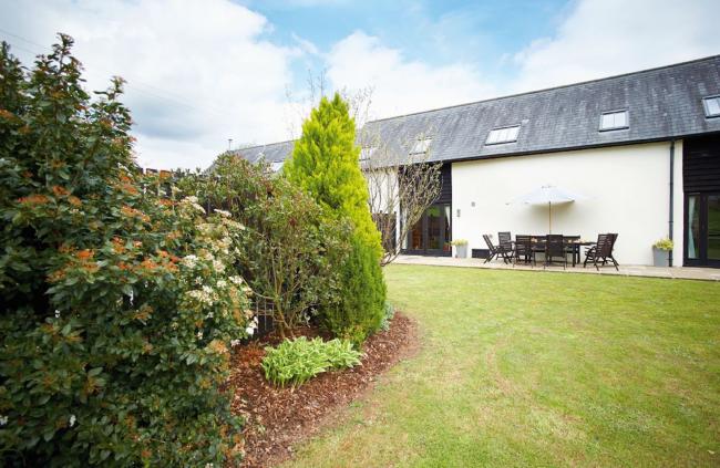 A barn conversion with Velux windows in the roof overlooks a large lawn.