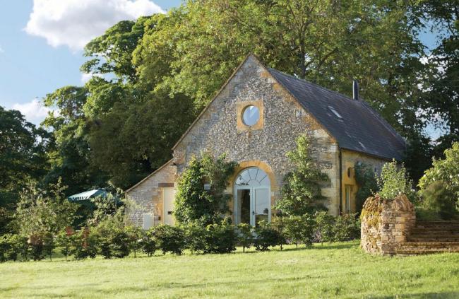 A coach house conversion with tall trees behind and a lawn in front.
