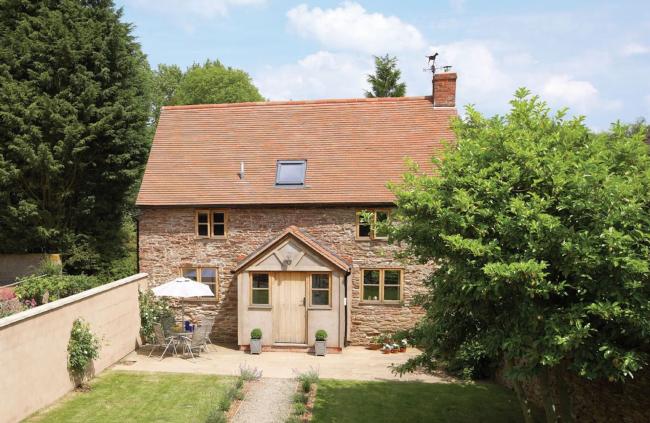 A stone-built cottage with enclosed porch overlooks a secure lawned garden
