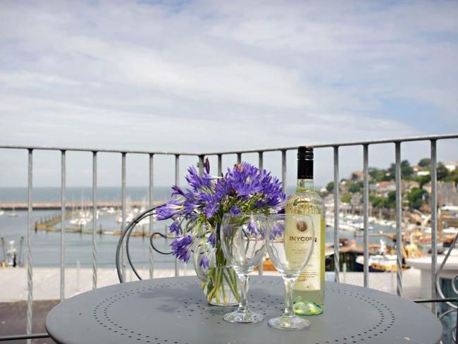 Behind a table set for cocktails on a balcony is a view of Brixham Harbour.