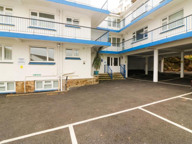 Exterior of an L-shaped apartment building with iron-railings protecting walkwabys and spaced for parking beneath.