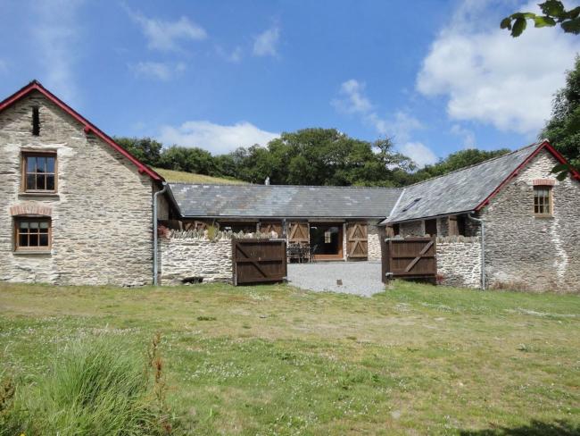 A twin-gabled Exmoor barn conmverion surounded by a lawn.