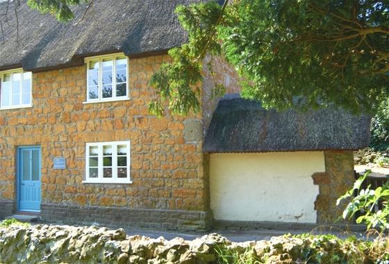 A honey-stone, thatched country cottage with a walled front garden.