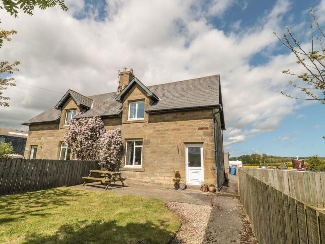 A semi-detached stone farm cottage with a lawn and picnic table.