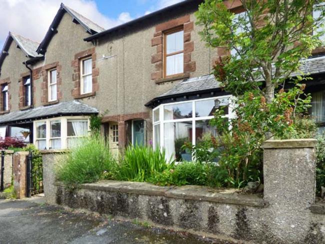 A 2-storey, terraced house with a large groundfloor bay window and a shrub-filled front garden.