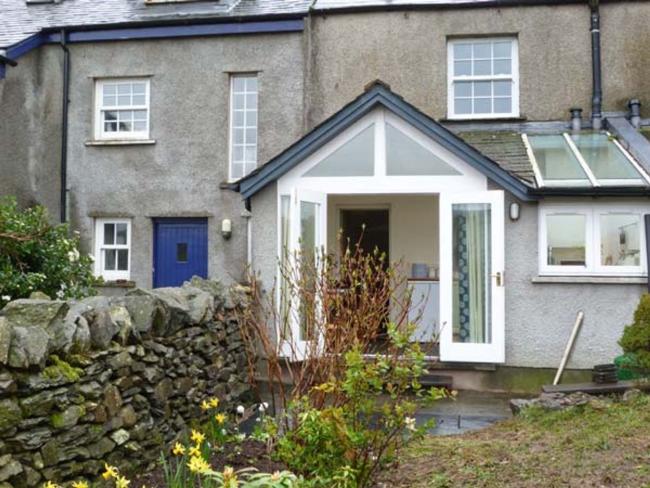 Rear exterior of a terraced holiday cottage in Ulverton overlooking a garden with flowering bulbs.