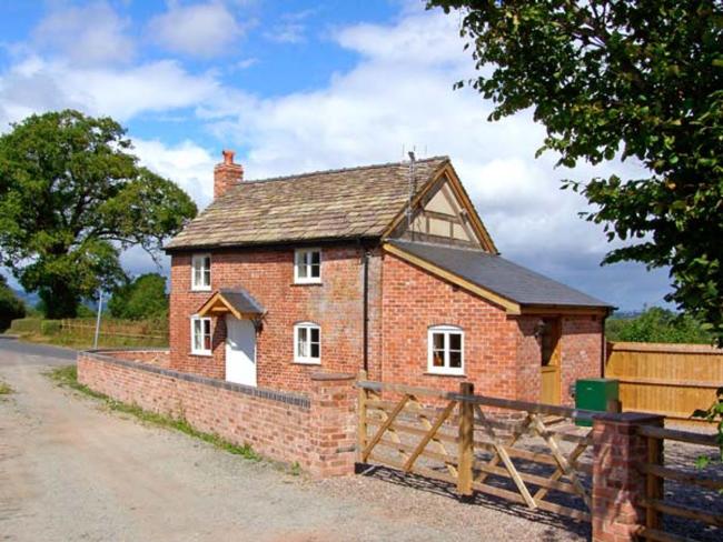 A red brick Herefordshire holiday cottage with a ground floor extension is surrounded by a low tone wall