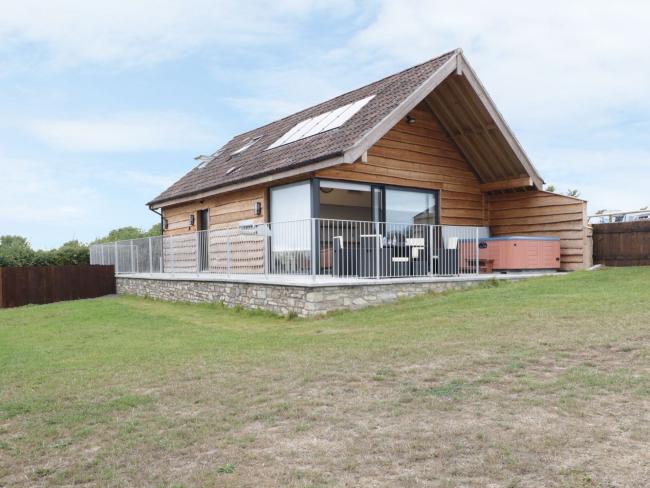 A large wooden Somerset holiday lodge with a hot tub on a sheltered deck overlooking a spacious lawn.