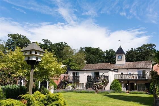A 2-storey house with a central clocktower and a long 1st-floor deck overlooking a spacious lawn.