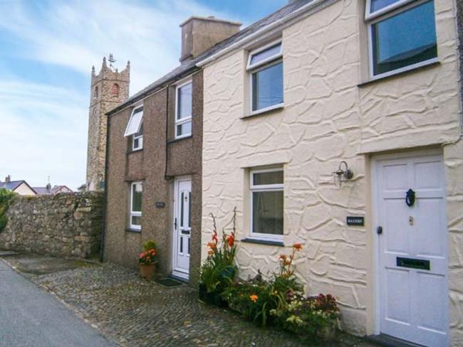A rendered holiday cottage overlooking a quiet lane near a church.