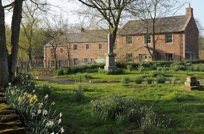 Exterior of a large country house surrounded by lawned gardens.