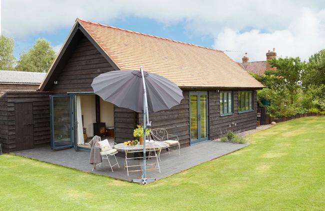 A single-storey clapperboard barn conversion with a patio and well-kept lawn.