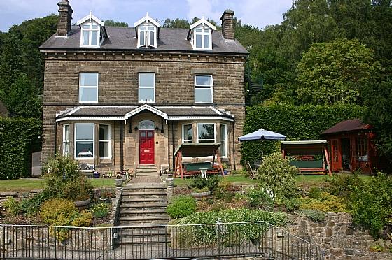 Exterior of a stone-built, 3-storey detached house  in front of a wood and overlooking a terraced garden