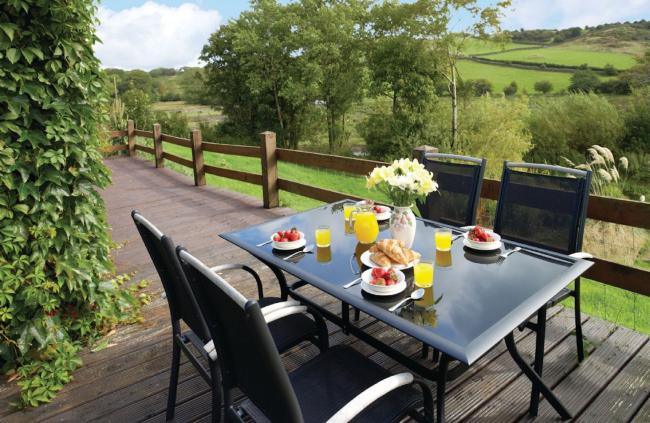 Fellside Barn Near Ulverston. An outdoor table for four on a wooden deck with views across a lawn and the Cumbria countrysideoutdoor